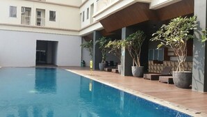 A swimming pool with a wooden deck, potted plants, and outdoor seating. - Mahogany x Sagita Karawang by Zuzu (Karawang)