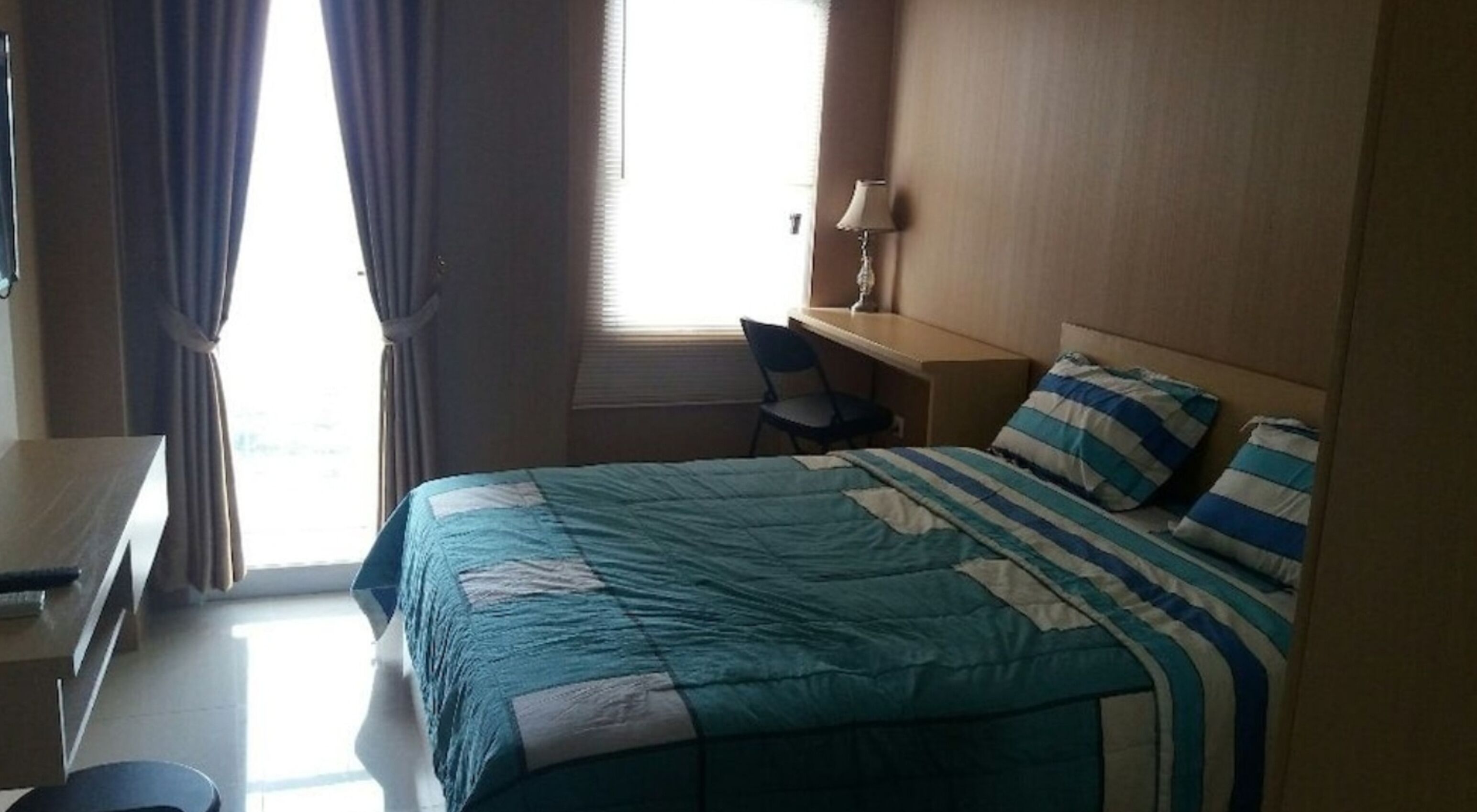 A hotel room with a bed, a desk, a chair, and a lamp.