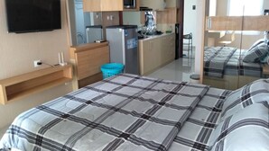 A compact hotel room with a bed, a TV, a kitchenette, and a bathroom. - Mahogany x Sagita Karawang by Zuzu (Karawang)