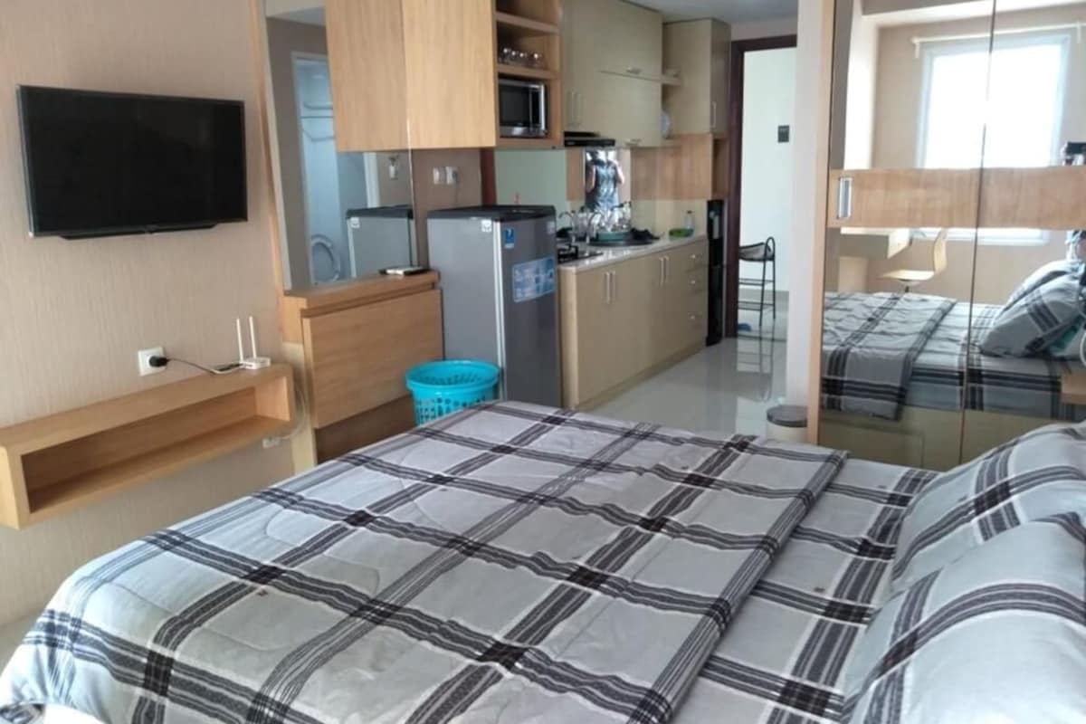 A bedroom with a bed, a TV, and a kitchenette with a microwave, refrigerator, and sink.