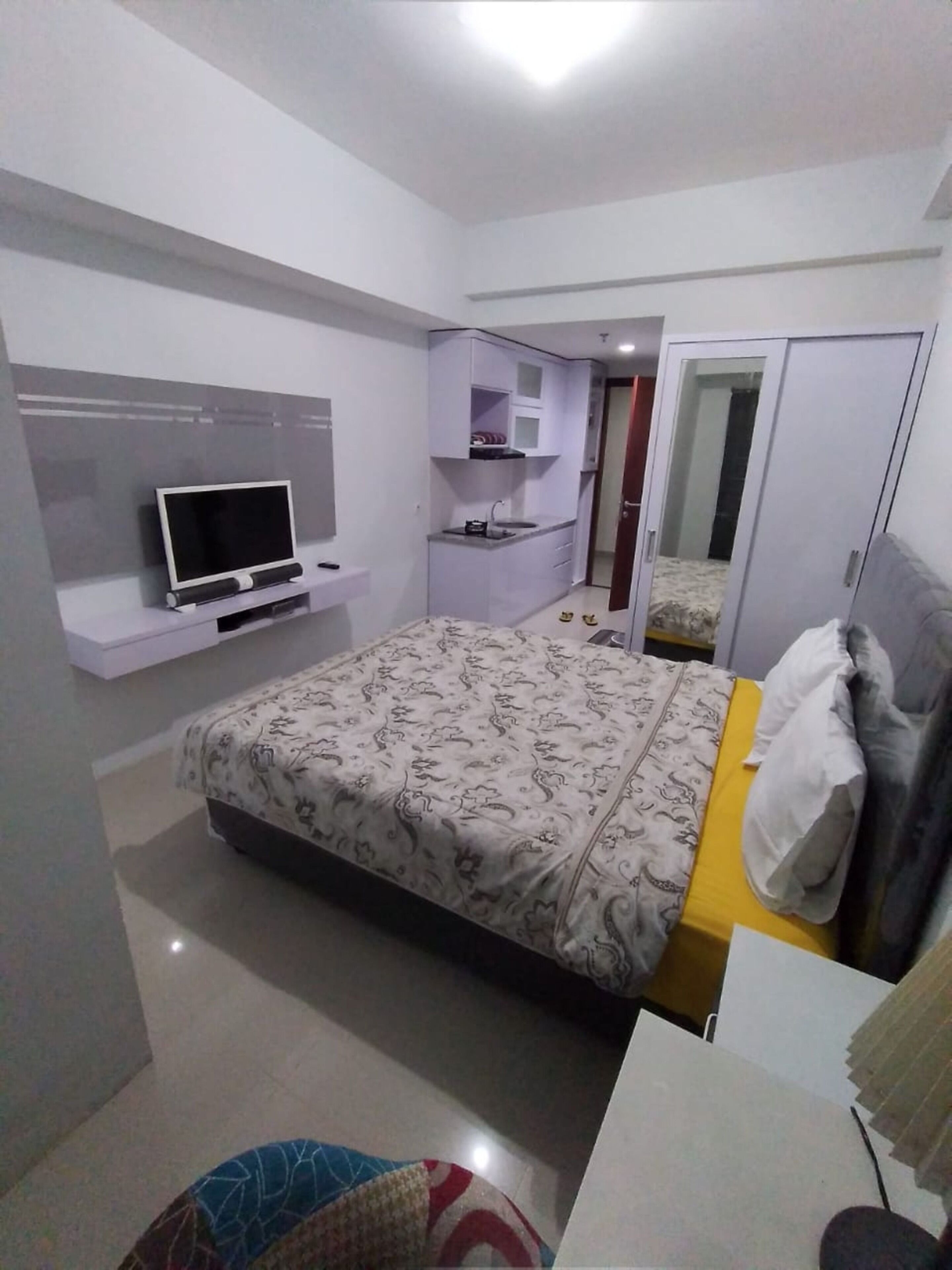 A bedroom with a bed, a TV on a shelf, a wardrobe, and a mirror.