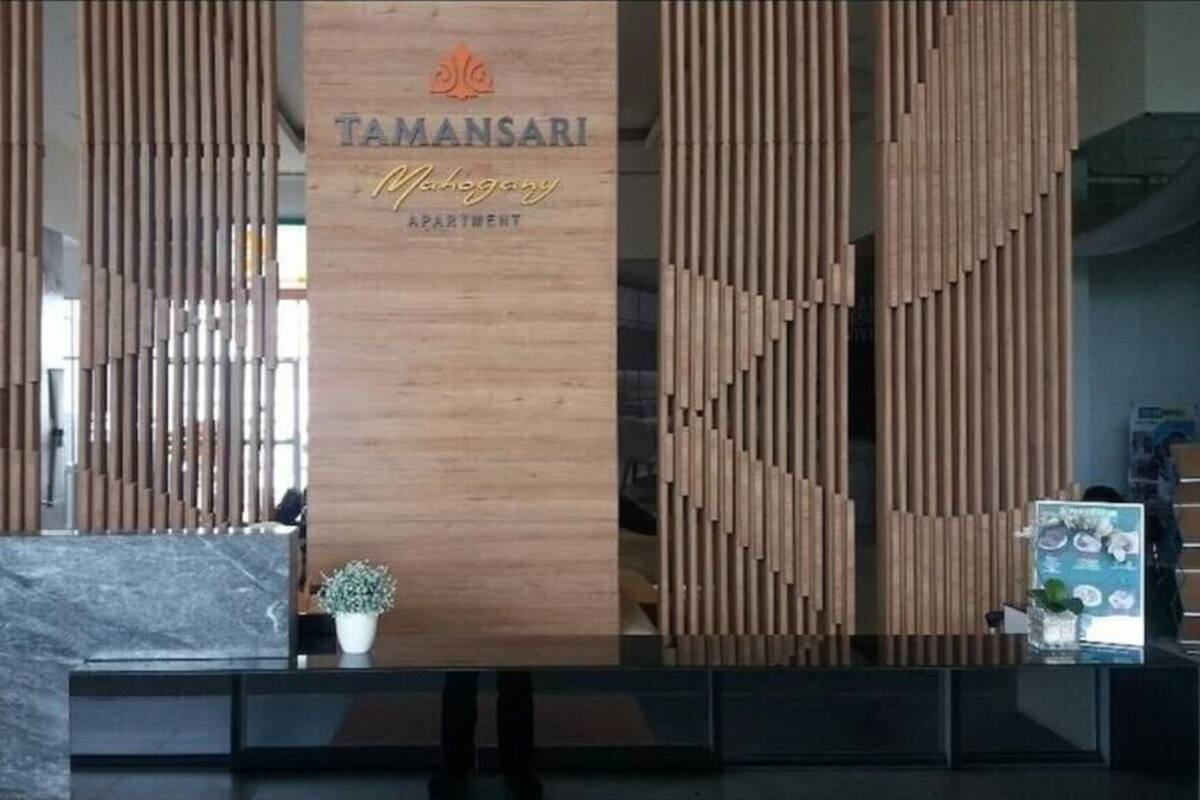 Un espace d’accueil agrémenté de panneaux en bois, d’une enseigne indiquant « TAMANSARI, appartements en acajou », et d’un comptoir de réception orné d’une plante en pot.