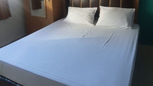 A neatly made bed with a headboard, a mirror on the wall, and a patterned wall behind the bed.