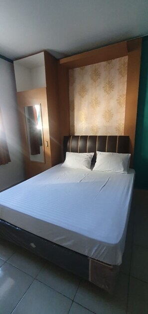 A neatly made bed with a headboard, a mirror on the wall, and a patterned wall behind the bed. - Rumah Dempo Syariah (Pontianak)