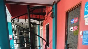 A dining area with a red table and wooden chairs, a spiral staircase, and a window with a metal grill.