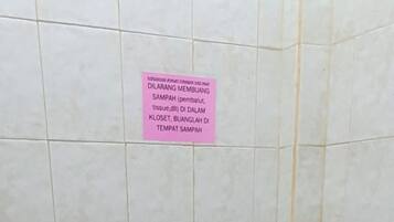 Eine Toilette mit einem rosafarbenen Schild darüber, einem gefliesten Boden und einer Wand mit einem vertikalen Riss.