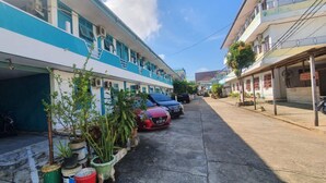 A narrow street with parked cars and potted plants along the sidewalk.
