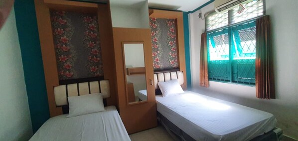 A bedroom with two single beds, a mirror, and a window with a green metal gate. - Rumah Dempo Syariah (Pontianak)