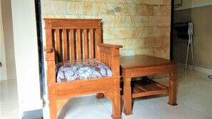 A wooden chair with a cushioned seat and backrest, placed on a tiled floor against a stone wall. - Hotel Abad Baru 1 (Pangandaran)