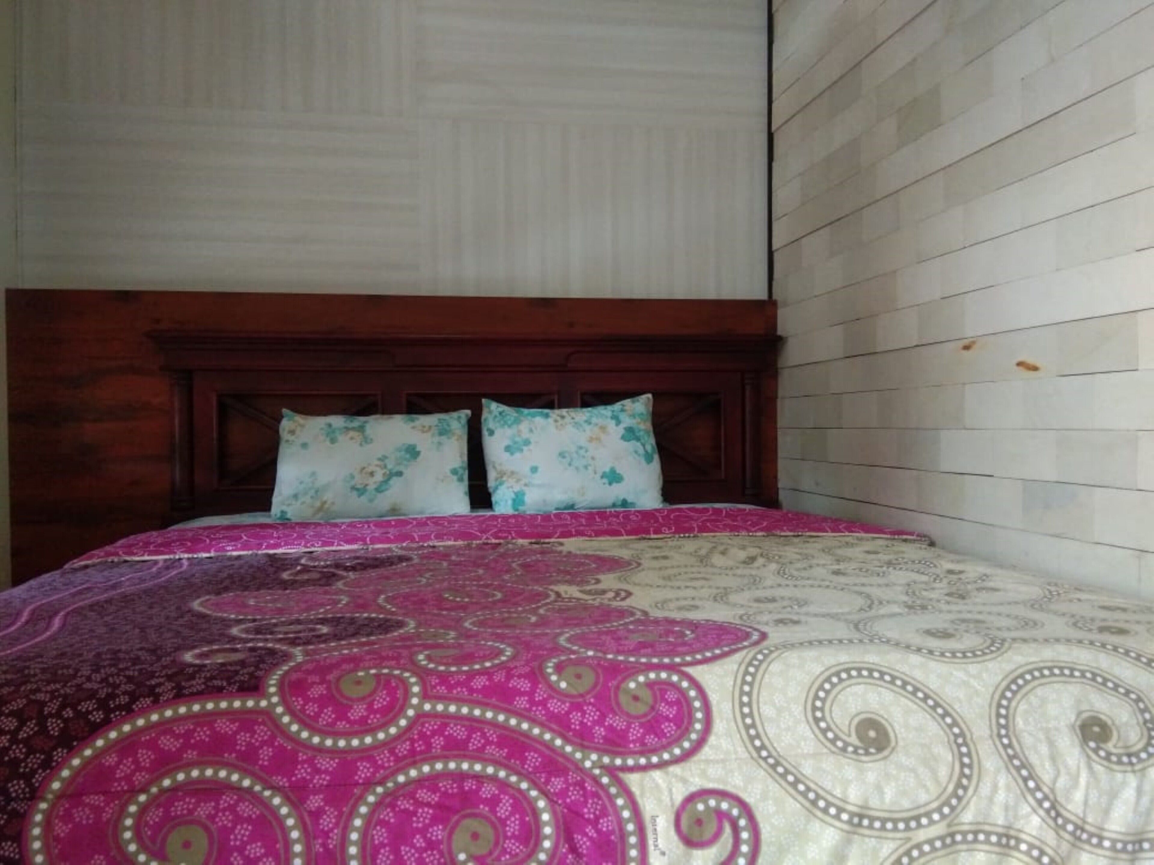 Een bed met een bloemenprintdeken en twee passende kussens, geplaatst tegen een houten hoofdbord en witte betegelde wanden.