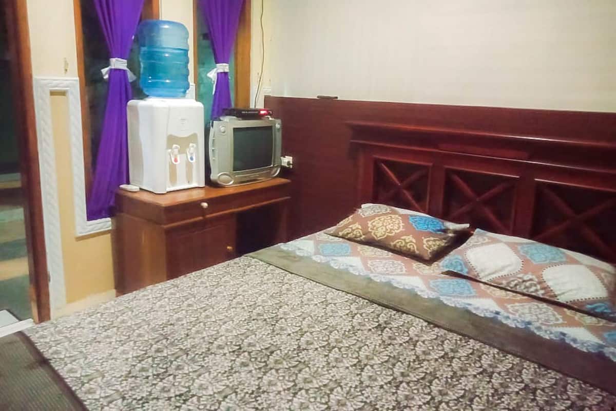 Habitación de hotel con cama, un pequeño televisor, dispensador de agua y cortinas moradas.