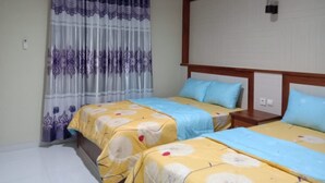 A hotel room with two beds, each with a floral bedspread, a wooden headboard, and a window with purple and white curtains. - Hotel Abad Baru 1 (Pangandaran)