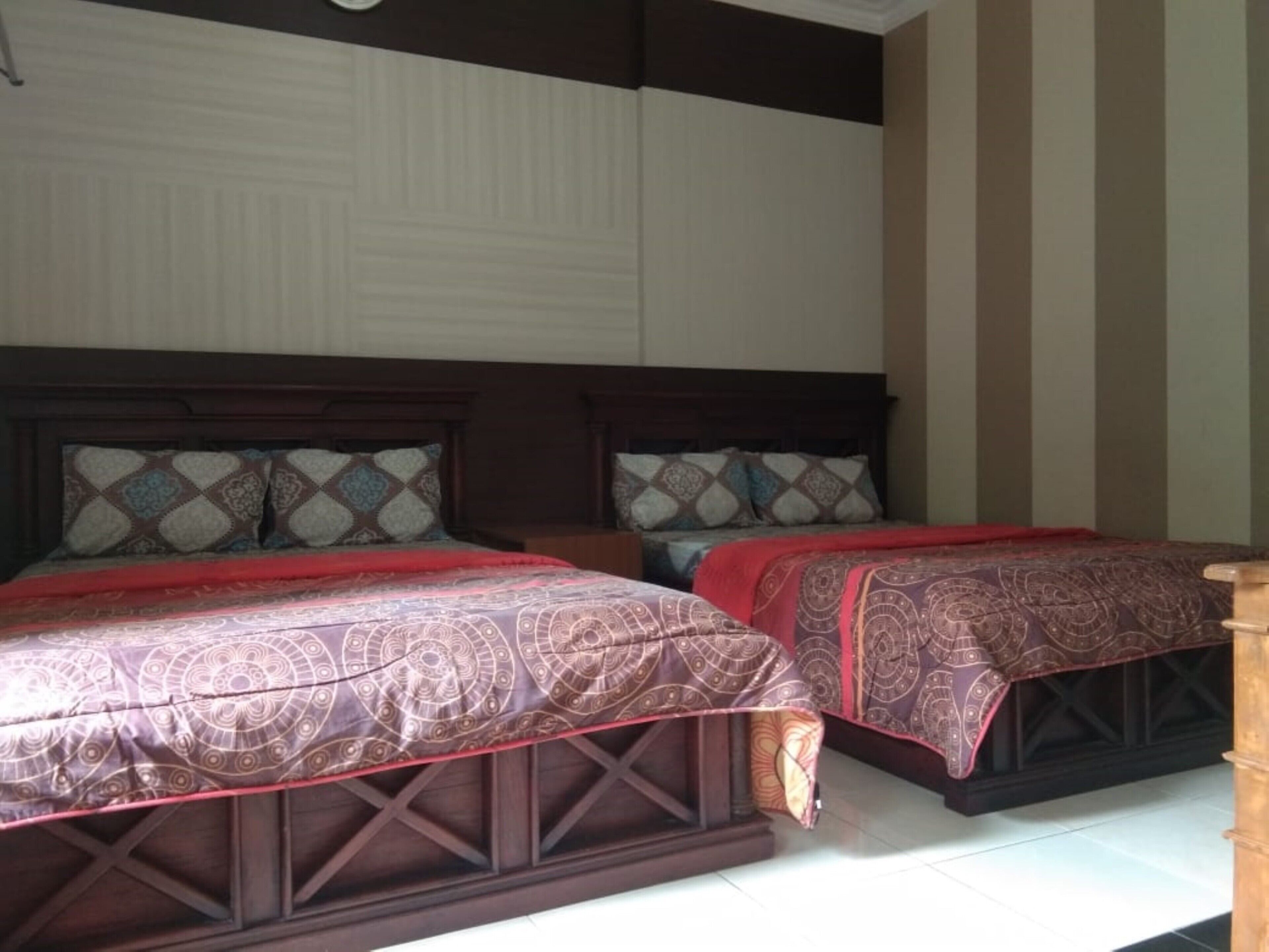 A double bed with a patterned bedspread and matching pillows, a wooden headboard, and a bedside table.