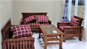 A cozy room with a wooden sofa set, a glass-top coffee table, and matching cushions. - Hotel Abad Baru 1 (Pangandaran)