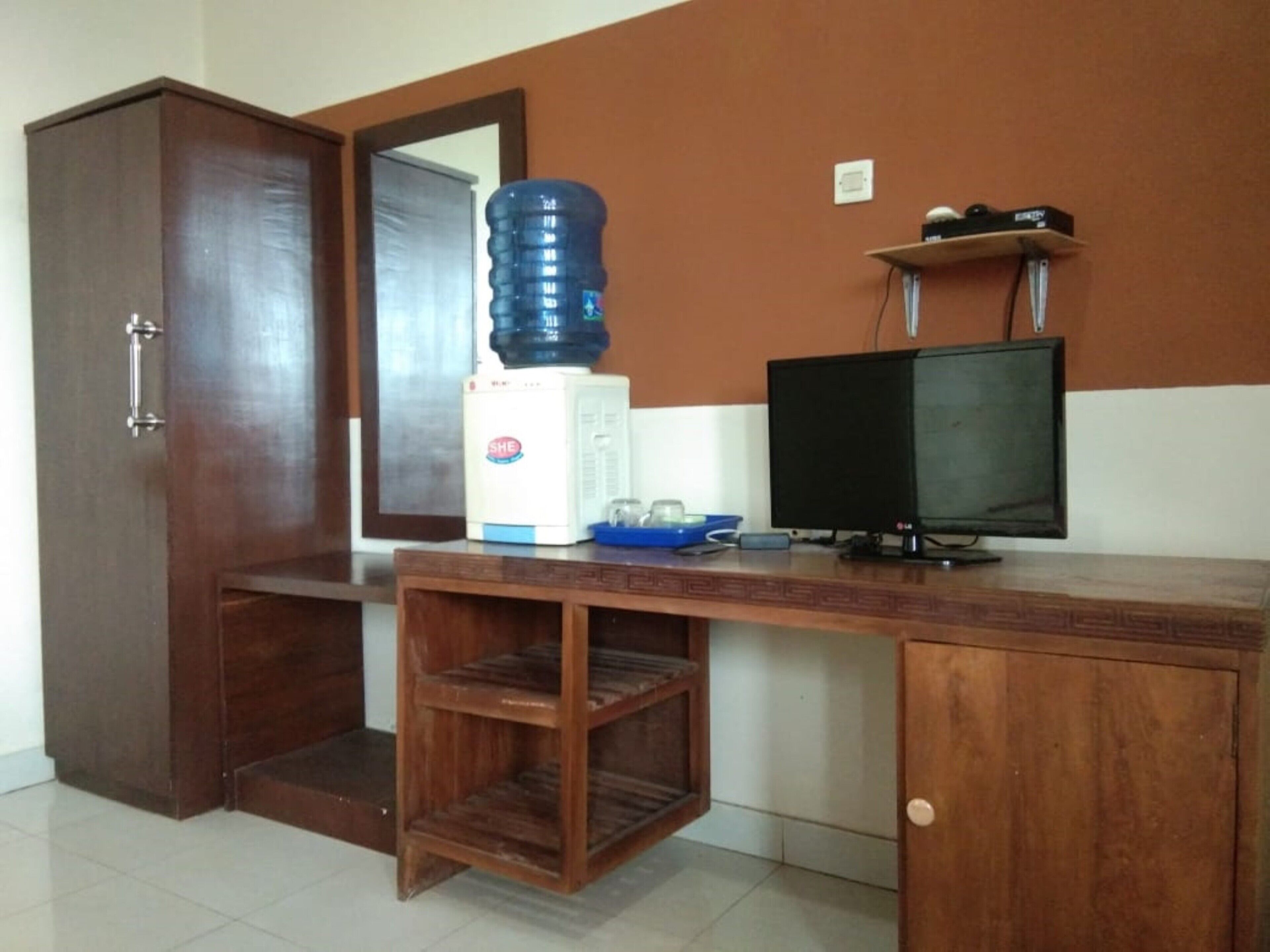 Une pièce comprenant un bureau en bois, un distributeur d’eau, un téléviseur et une armoire.