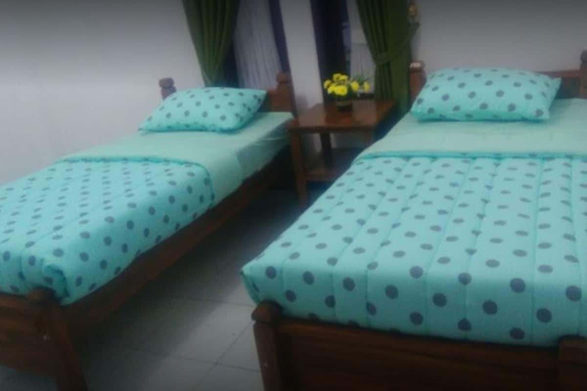 Dos camas individuales con ropa de cama azul a lunares a juego, cabeceras de madera y una pequeña mesa con un jarrón de flores amarillas entre ellas.