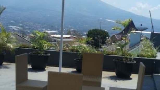 Un espacio de estar al aire libre techado, con sillas de mimbre y plantas en macetas, con vistas a un paisaje urbano y una montaña.