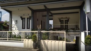 Una casa de dos pisos con balcón, entrada protegida por un portón y plantas en macetas.