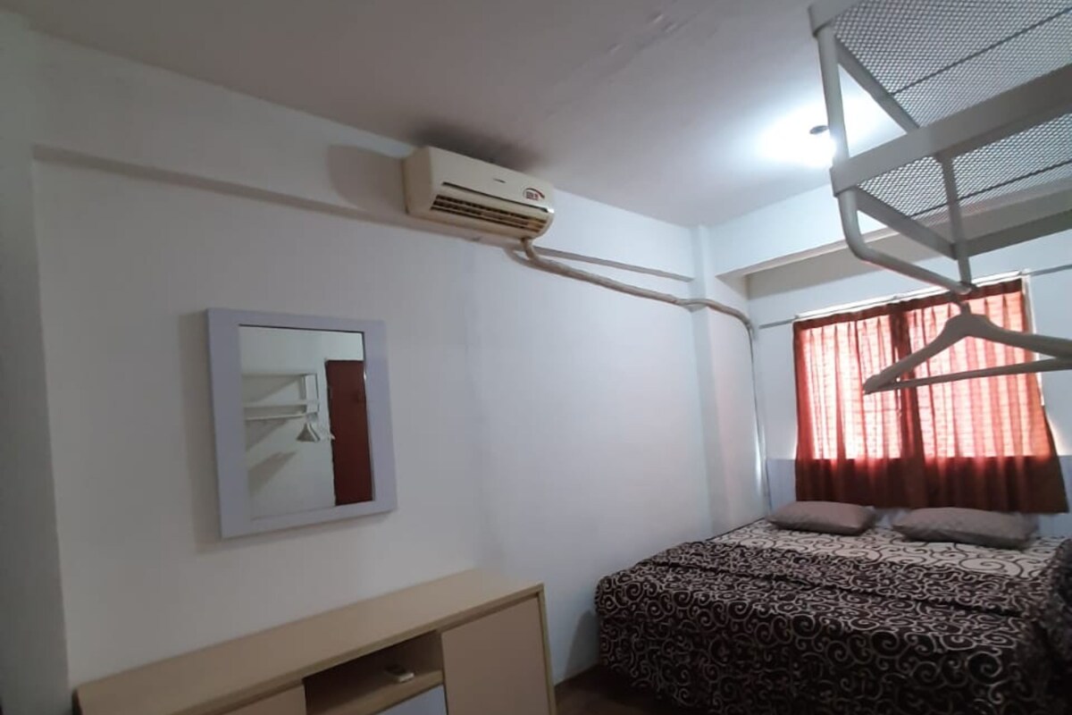A bedroom with a bunk bed, a desk with drawers, a wall-mounted air conditioner, a framed picture, and a window with curtains.