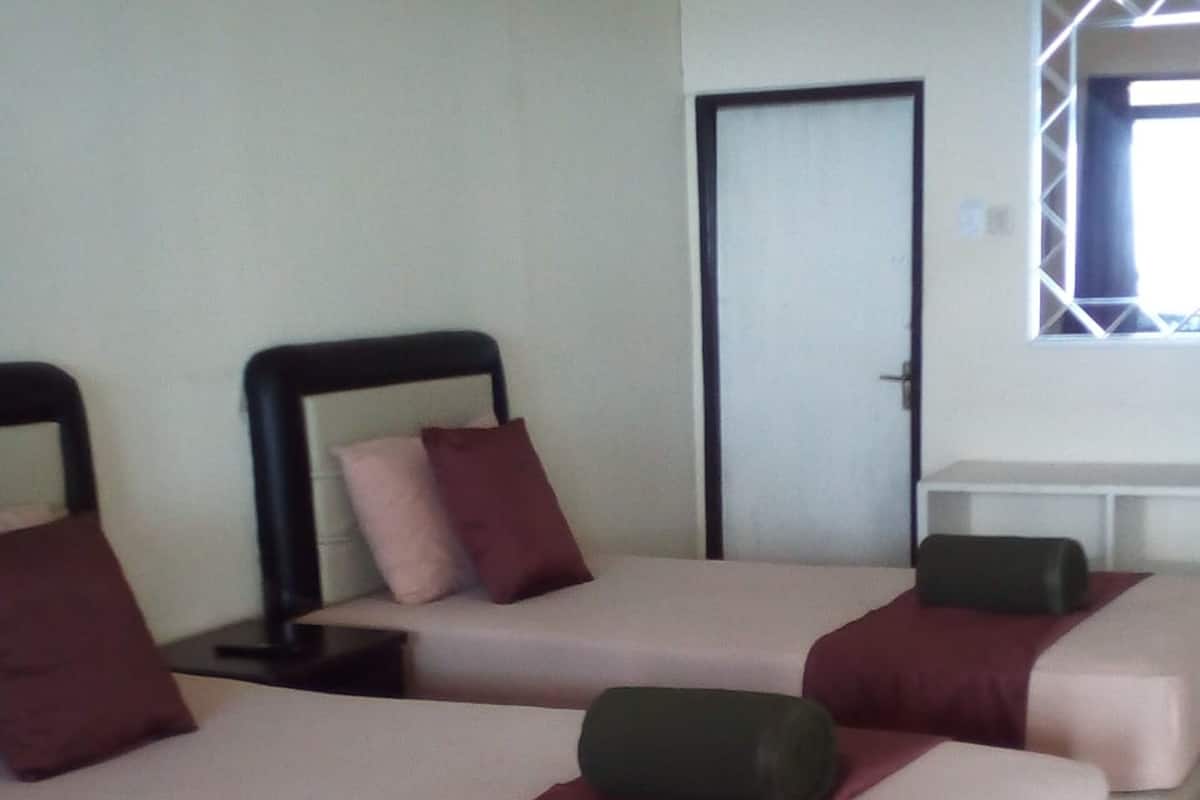 Una camera d'albergo con due letti, ciascuno con testiera, cuscini e coperta. Si vede una finestra con vista sull'esterno.