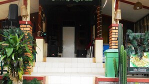 Een gebouwtrappe leidt naar een deur, omringd door planten en een bord met de tekst 'd Cunang Caffe & Resto'.