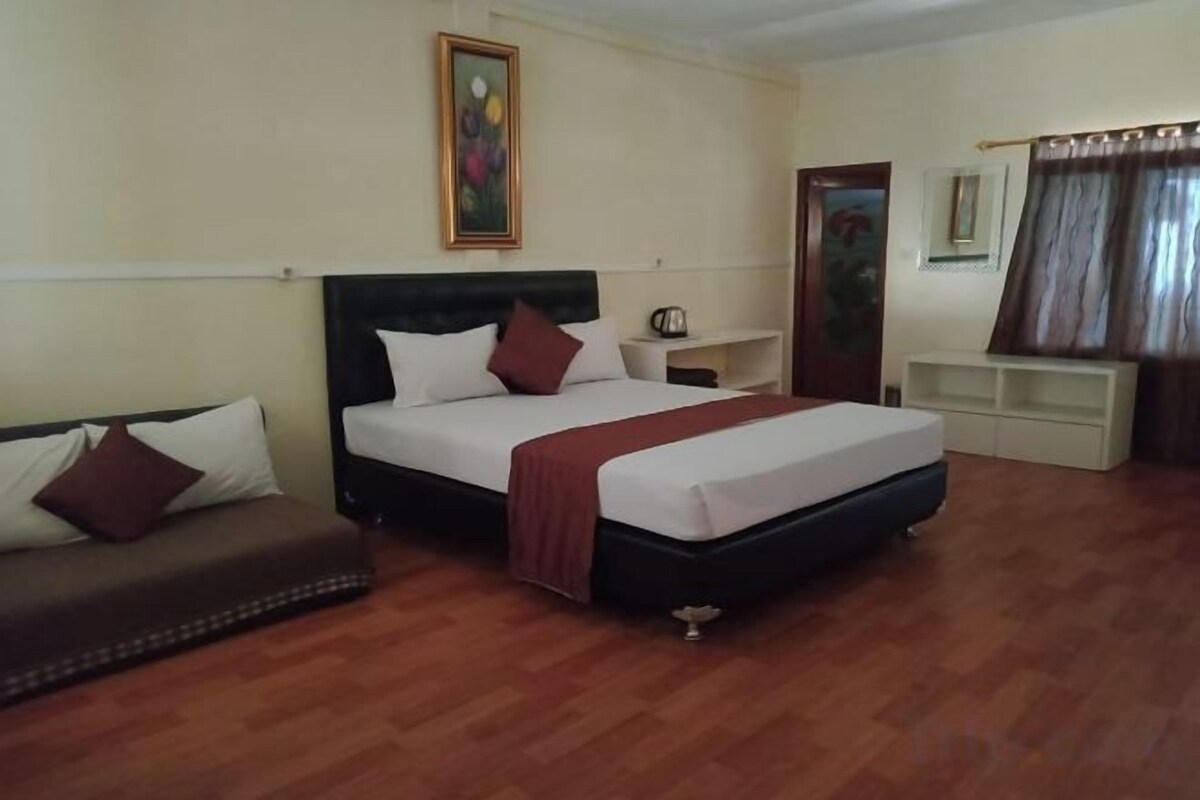 A hotel room with a bed, a sofa, a bedside table, and a mirror.