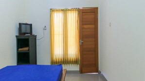A room with a bed, a TV on a shelf, a door, and a window with curtains. - Pondok Wisata Intan Indah 1 (Denpasar)