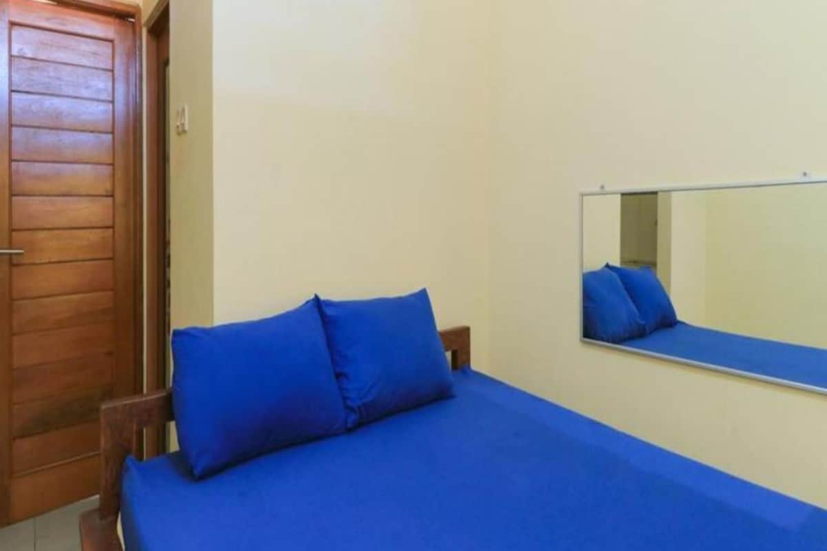 A bedroom with a wooden door, a bed with blue bedding, and a mirror on the wall.