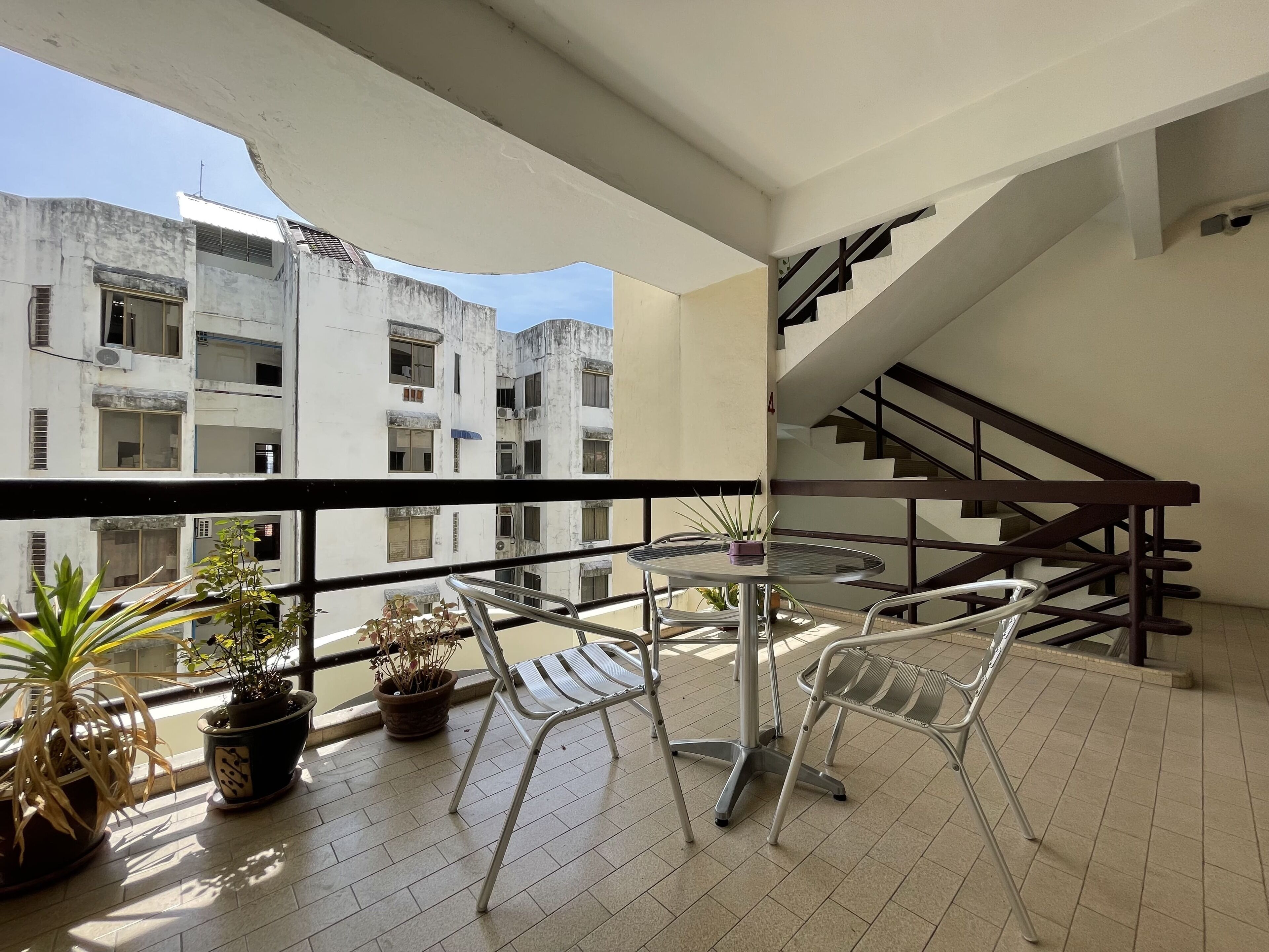 A balcony with a round table and two chairs, potted plants, and a view of a multi-story building with balconies.