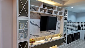 A modern living room with a large flat-screen TV mounted on a wall with a marble pattern. There are built-in shelves with decorative items and a small table with a vase of flowers. - @Saphan Pla Bangkok (Bangkok)