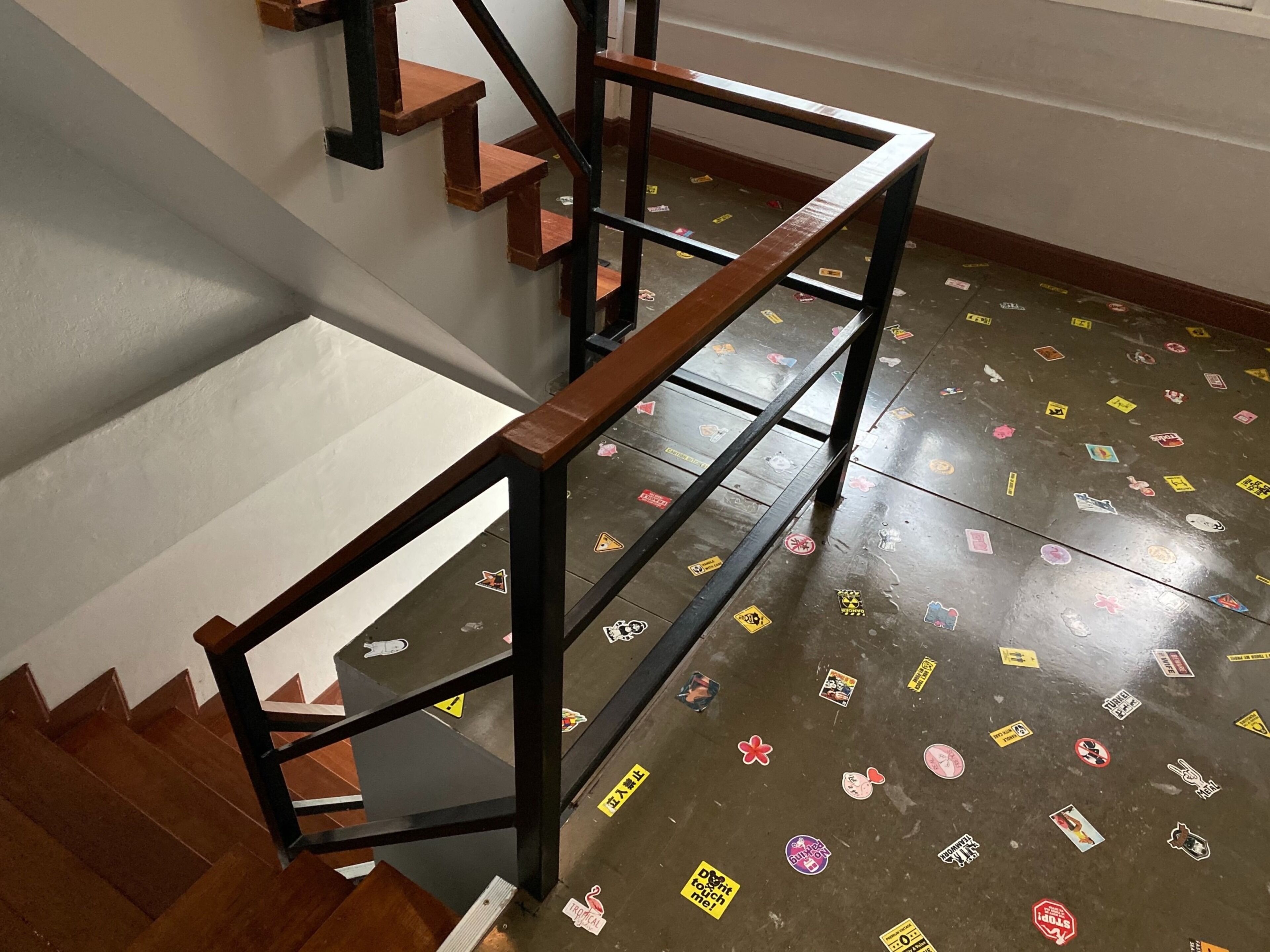 A staircase with wooden steps and metal railings, leading to a landing with a tiled floor decorated with various stickers.