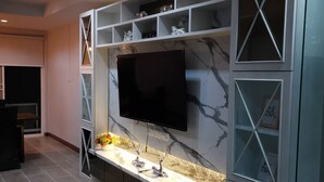 A modern living room with a large flat-screen TV mounted on a marble-patterned wall, surrounded by built-in shelves and decorative items. - @Saphan Pla Bangkok (Bangkok)