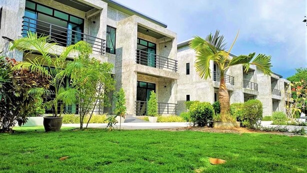 A modern building with a flat roof, large windows, and a well-maintained lawn with palm trees. - Busaba House (Pattaya)