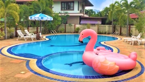 A swimming pool with a pink flamingo float, surrounded by lounge chairs and a house in the background. - Busaba House (Pattaya)