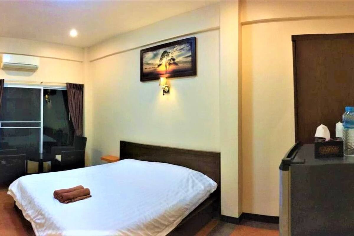 A hotel room with a bed, a desk, a chair, a picture on the wall, and a water bottle on the desk.