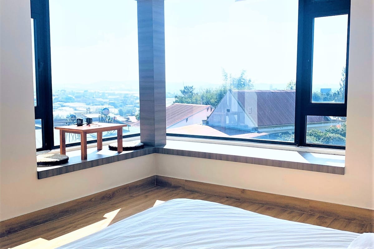 Un dormitorio con un ventanal grande, una cama y una pequeña mesa con sillas.