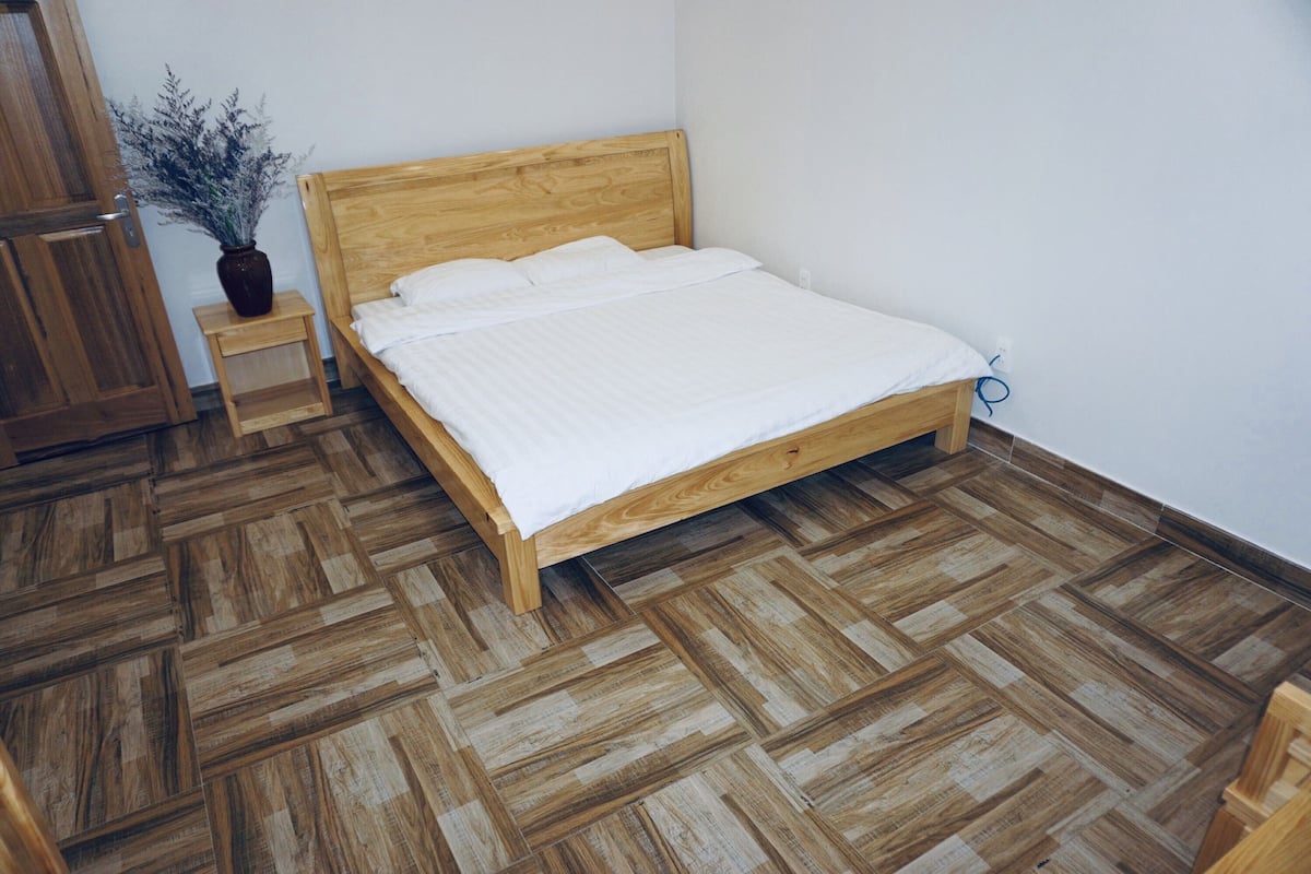 Una cama de madera con ropa blanca en una habitación con suelo de diseño espiga.