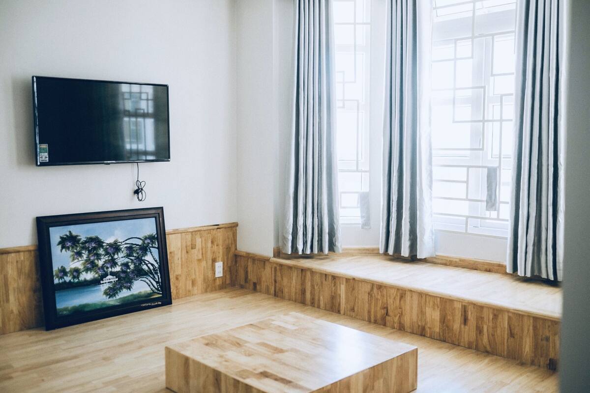 Una sala de estar moderna con una televisión de pantalla plana montada en la pared, un banco de madera junto a la ventana y una mesa de centro de madera en el centro.