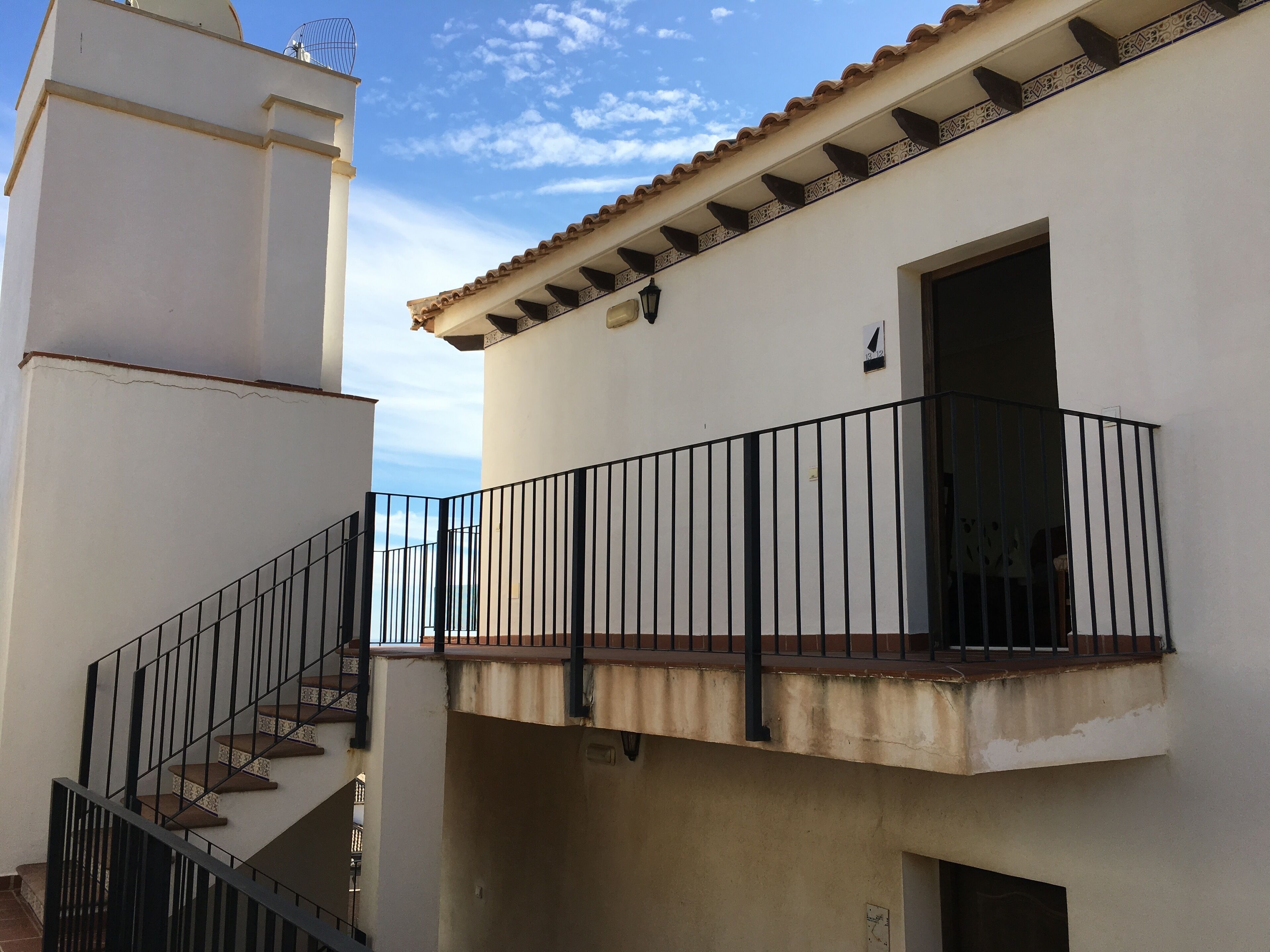 A building with a white exterior, a balcony with a black railing, and a staircase leading to an upper floor.