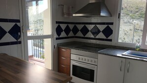 Een keuken met een gasfornuis, oven en een raam met uitzicht op een heuvelachtig landschap.