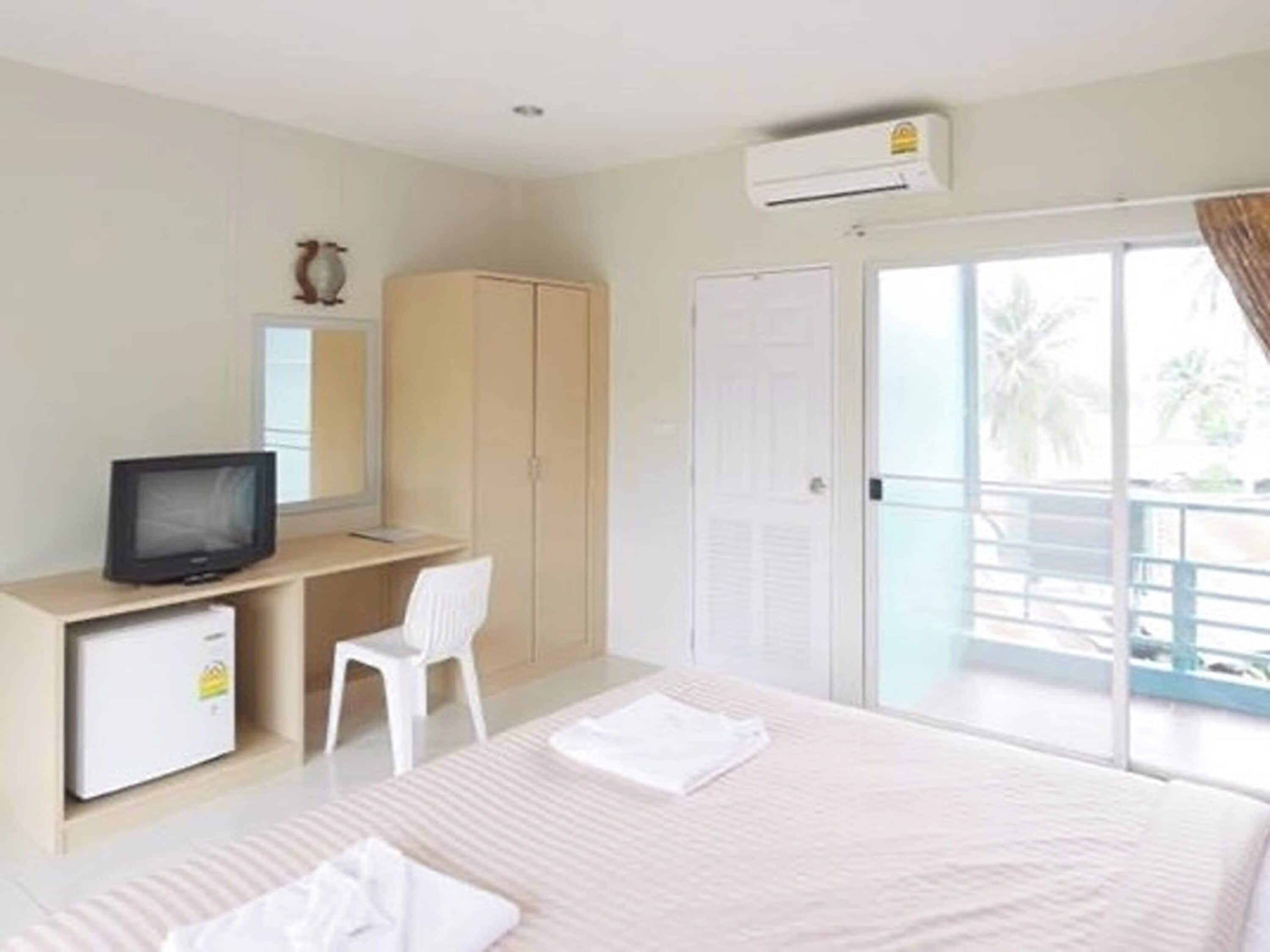 Habitación de hotel con cama, escritorio con televisor, armario y puerta corrediza de cristal que da a un balcón.