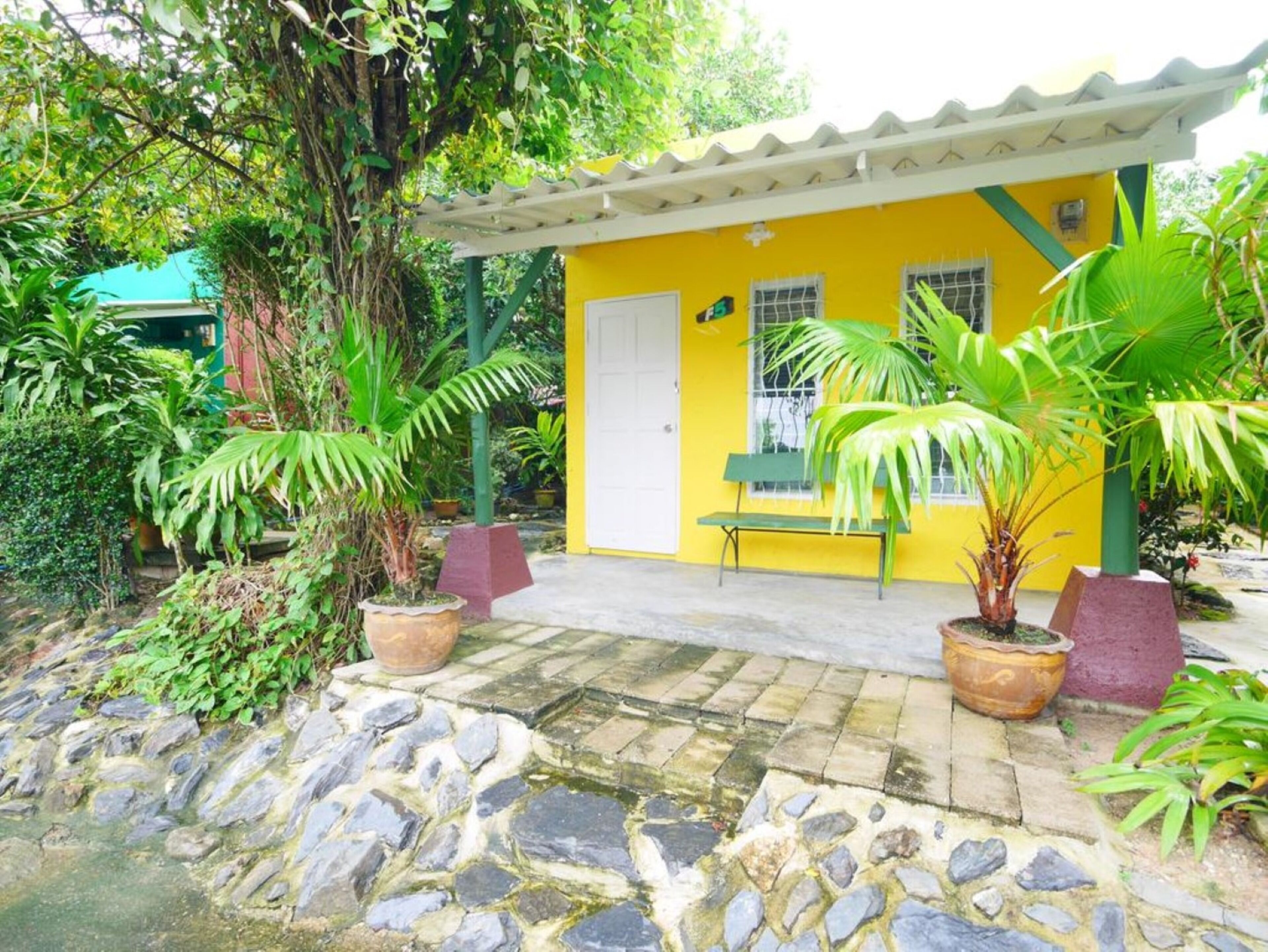 A small yellow building with a white door, a bench, and potted plants.