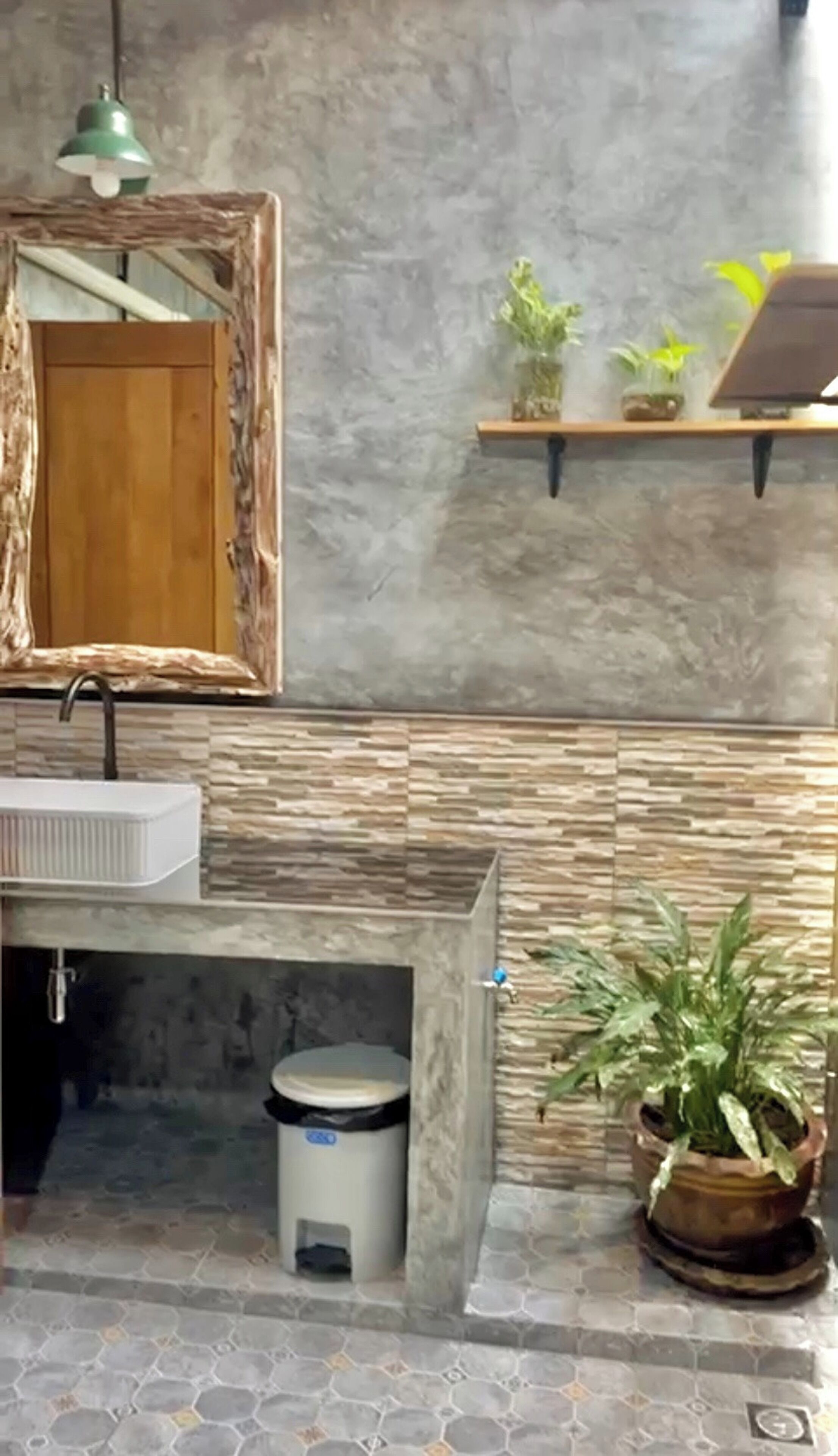 A bathroom with a rustic wooden vanity, a large mirror, a green pendant light, and potted plants on a shelf.