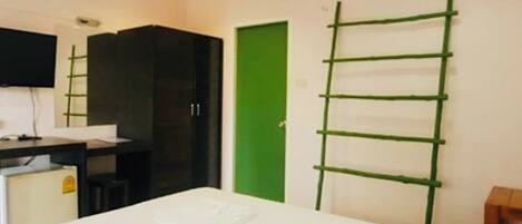 A hotel room with a bed, a desk, a chair, a wardrobe, a green door, and a ladder.