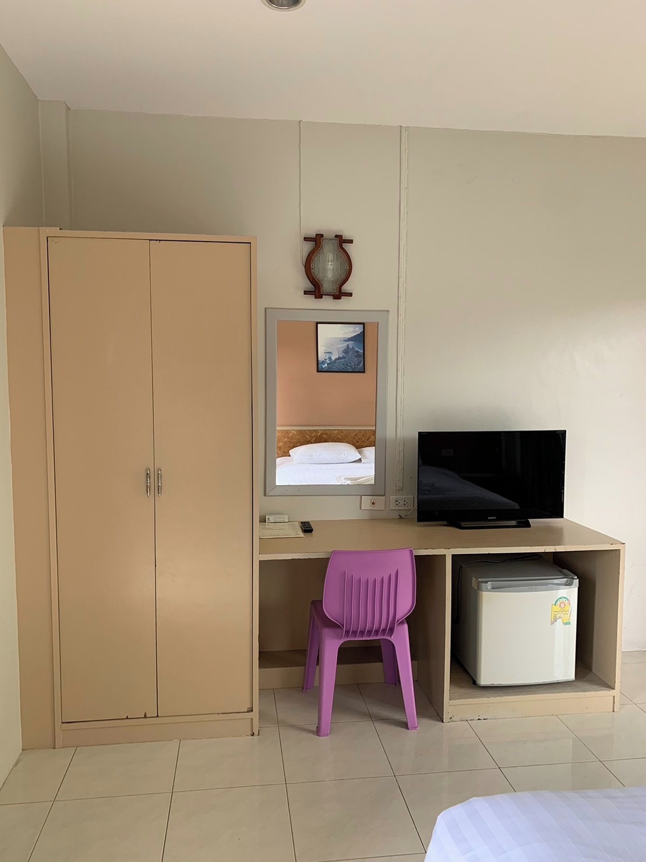 Une chambre à coucher comprenant un lit, un bureau avec un ordinateur, une télévision, une armoire et un petit réfrigérateur.