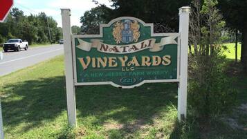 A sign for Natali Vineyards LLC, a New Jersey farm winery, with a road sign and a stop sign in the background.