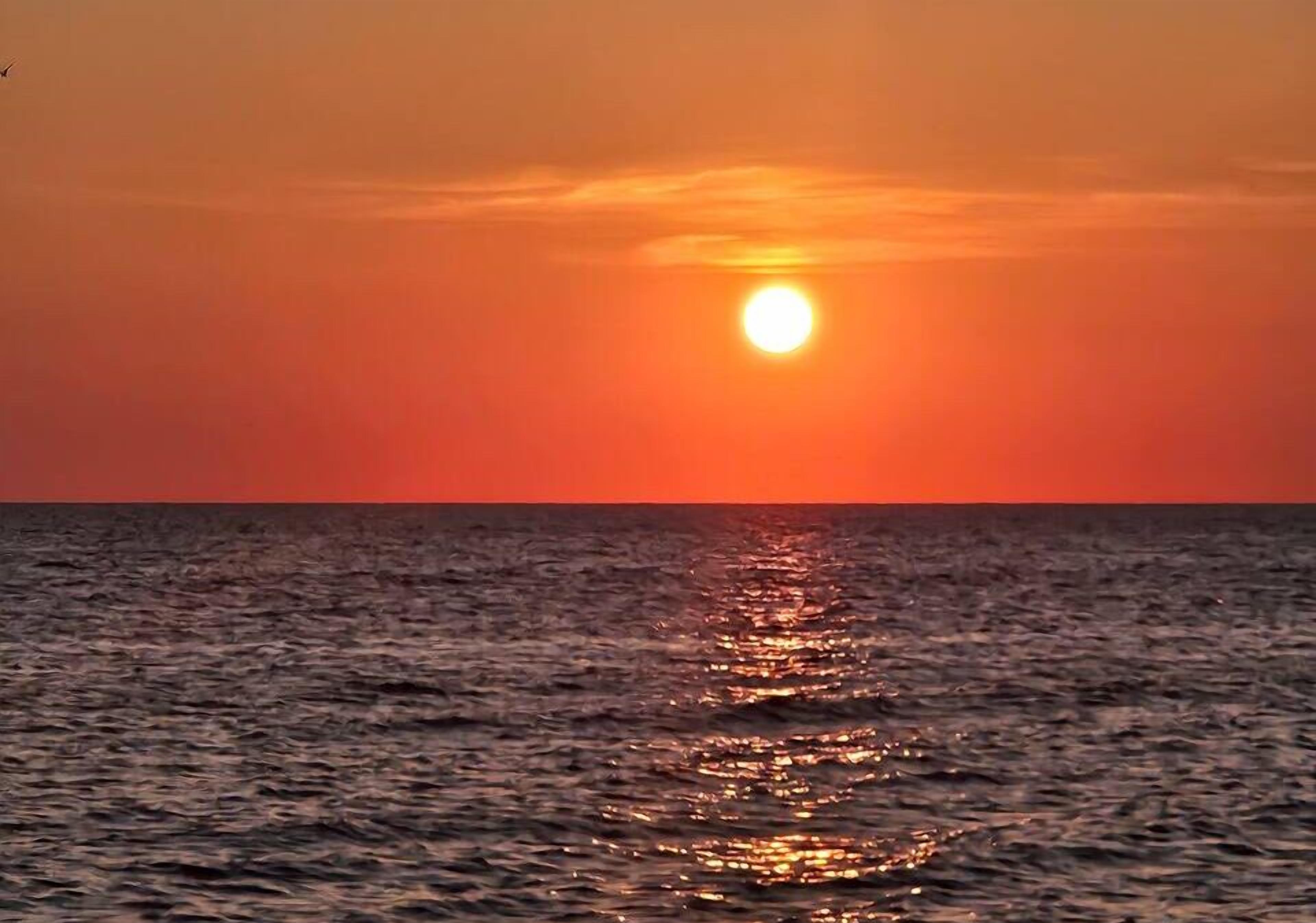 Un atardecer sobre el océano, con el sol reflejado en el agua.