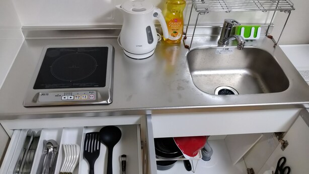 Una cocina con estufa, tetera, pileta y diversos utensilios.
