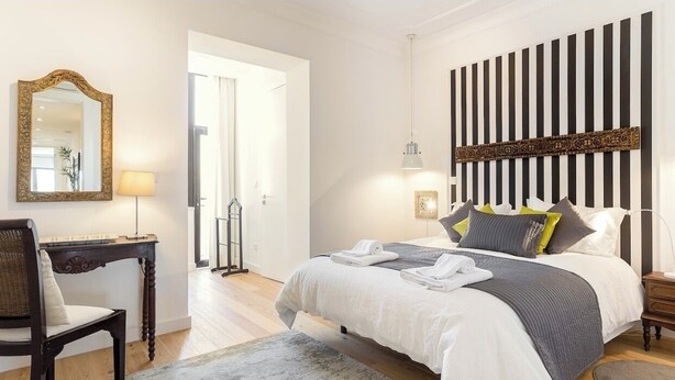 Ein modernes Schlafzimmer mit einem großen Bett, einem Schreibtisch mit Stuhl, einem Spiegel und einer dekorativen Wandverkleidung.