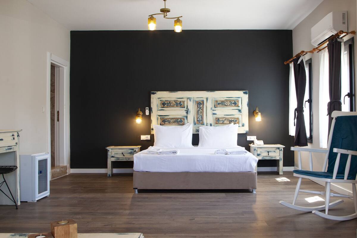 A bedroom with a large bed, bedside tables, a chair, a desk, and a wall-mounted air conditioner.